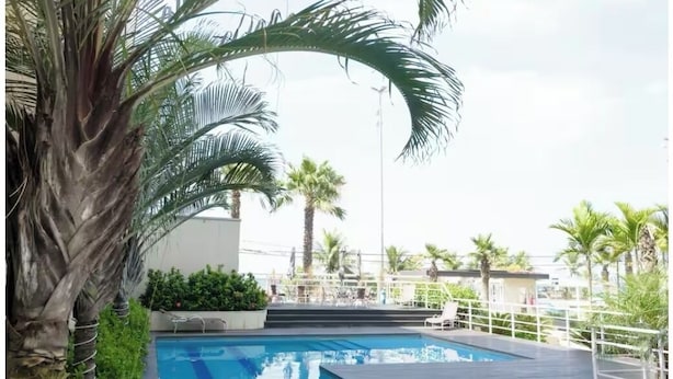 A swimming pool with a wooden deck, surrounded by palm trees and a white fence. - PEPÊ BEACH APARTMENT  (Barra da Tijuca Rio de Janeiro)