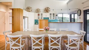 Uma cozinha moderna com armários brancos, uma ilha de madeira e um espaço de refeições com cadeiras brancas.