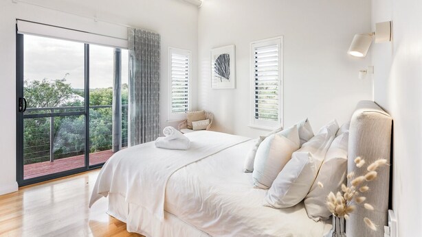 Quarto moderno com uma cama grande, vista para o verde pela janela e porta deslizante para área externa.