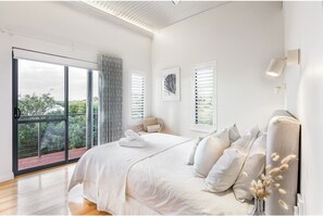 Ein modernes Schlafzimmer mit einem großen Bett, Blick auf Grün hinter dem Fenster und einer Schiebetür zu einem Außenbereich.