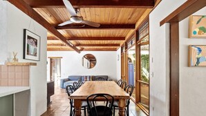 A dining area with a wooden table and chairs, a ceiling fan, and a view through a glass door. - The Bower House | Margaret River (Margaret River)