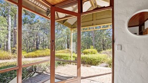 A room with large glass doors leading to an outdoor area with a view of trees and a brick pathway. - The Bower House | Margaret River (Margaret River)