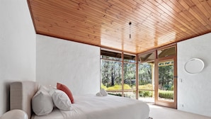A modern bedroom with a large bed, a wooden ceiling, and a view of a forest through glass doors. - The Bower House | Margaret River (Margaret River)