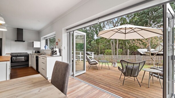 A modern kitchen with a large sliding glass door leading to an outdoor deck with wooden flooring, outdoor furniture, and a pergola.