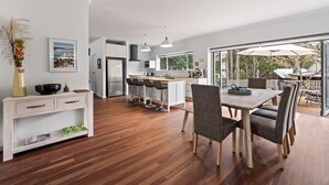 A modern kitchen with white cabinets, a central island with bar stools, and a dining area with a table and chairs.