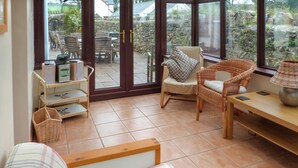 A cozy living area with a sofa, wicker chairs, a table, and a view through large glass doors to an outdoor patio with a stone wall and greenery. - 5 bedroom accommodation in Horton, near Gower (Horton, near Gower)