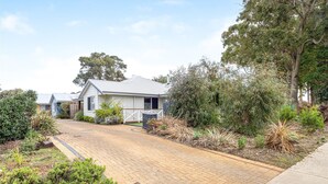 A single-story house with a paved driveway, surrounded by various shrubs and trees.
