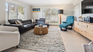 A modern living room with a sectional sofa, a blue armchair, a coffee table, and a TV on a wooden cabinet.