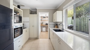 A modern kitchen with white cabinetry, a black refrigerator, a built-in oven, and a large window with a view of the outdoors.