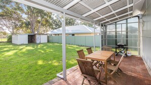Eine überdachte Terrasse mit Tisch, Stühlen, einem Grill und einem grünen Rasen.
