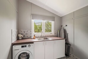 Une cuisine compacte équipée d’un lave-linge, d’un évier et d’une fenêtre donnant sur un espace verdoyant.
