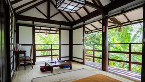 A traditional Japanese-style room with tatami flooring, a bed, a table, and a chair. - Griya De Sachi (Cepaka)