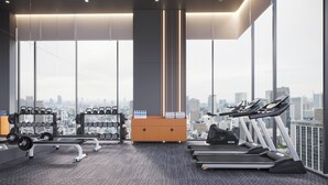 A modern gym with treadmills, dumbbells, and weight machines, large windows with a city view.