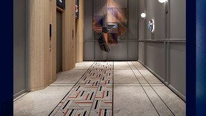 A modern hallway with a patterned floor, wooden paneling on one side, and a geometric light fixture on the ceiling.