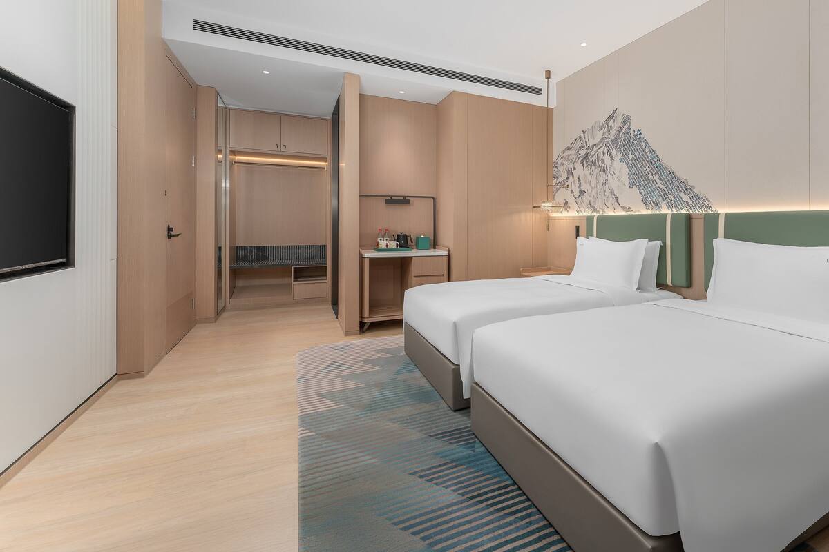 Une chambre d’hôtel avec deux lits, un bureau, un coin salon et une grande œuvre d’art accrochée au mur.