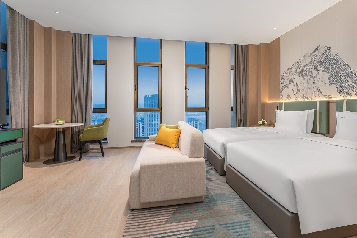 A hotel room with a bed, a desk, a chair, a small table, and a TV.