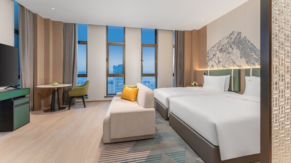 Quarto de hotel com cama, escrivaninha, cadeira, mesa pequena e televisão.