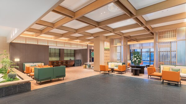 Eine geräumige Lobby mit hoher Decke, Holzbalken und einer Sitzecke mit orangefarbenen und grünen Sofas.