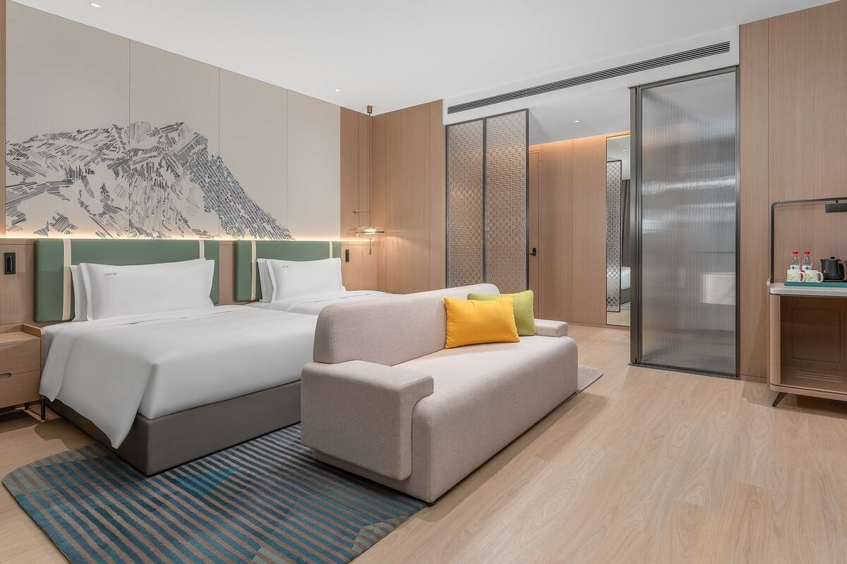 Une chambre d'hôtel moderne avec deux lits, un canapé, un bureau et une grande œuvre d'art accrochée au mur.
