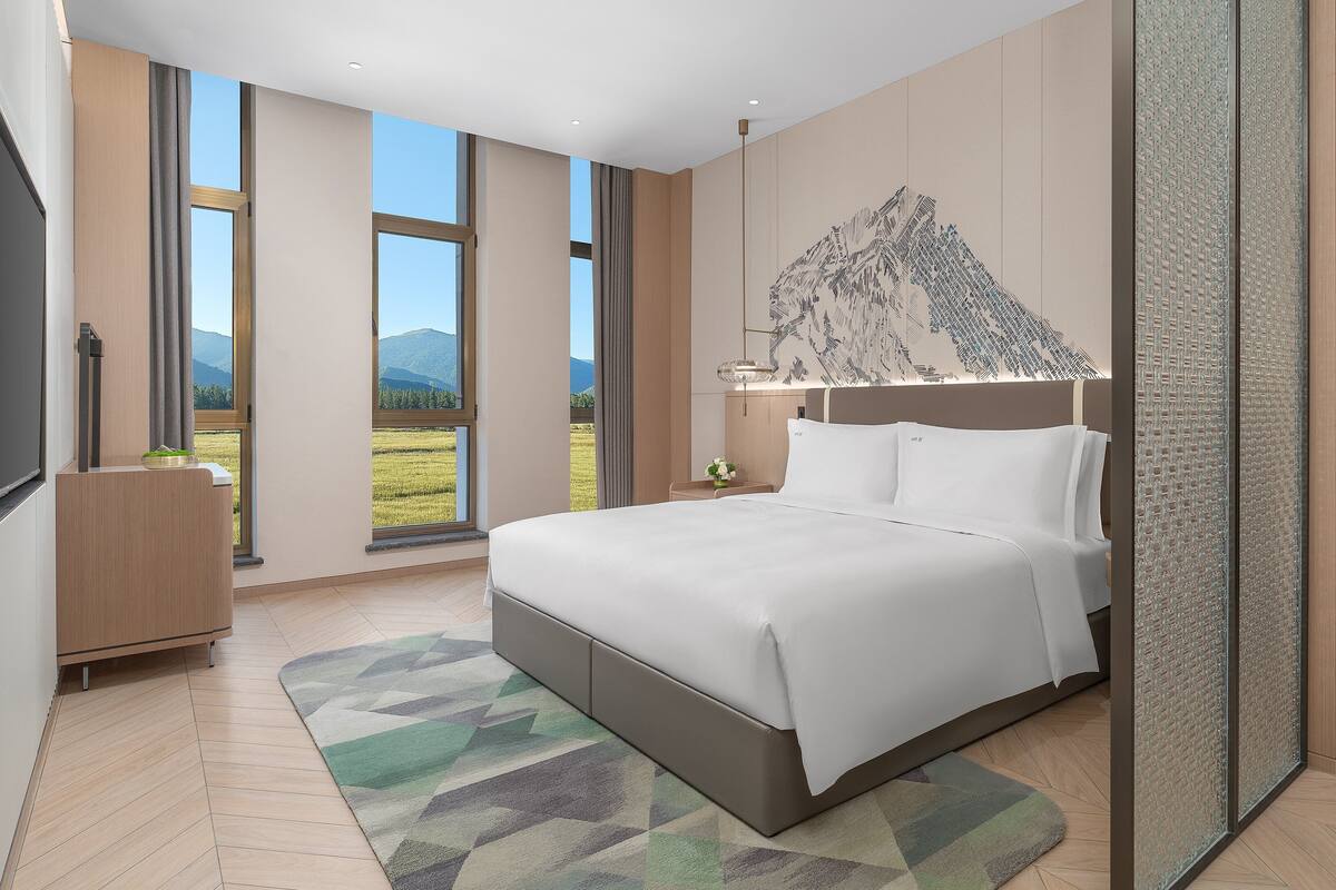 Une chambre moderne avec un grand lit, une vue sur un paysage montagneux et un élément décoratif mural.