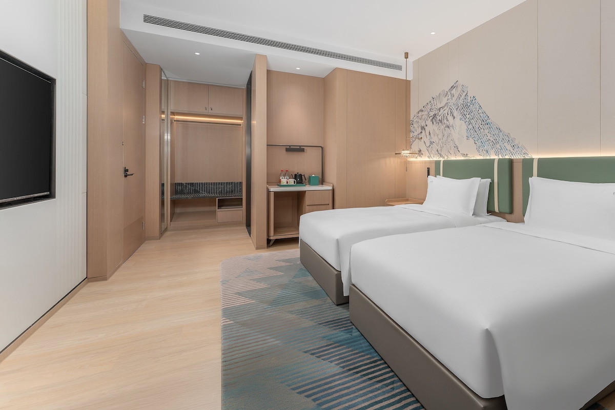 A hotel room with two beds, a desk, a seating area, and a large artwork on the wall.