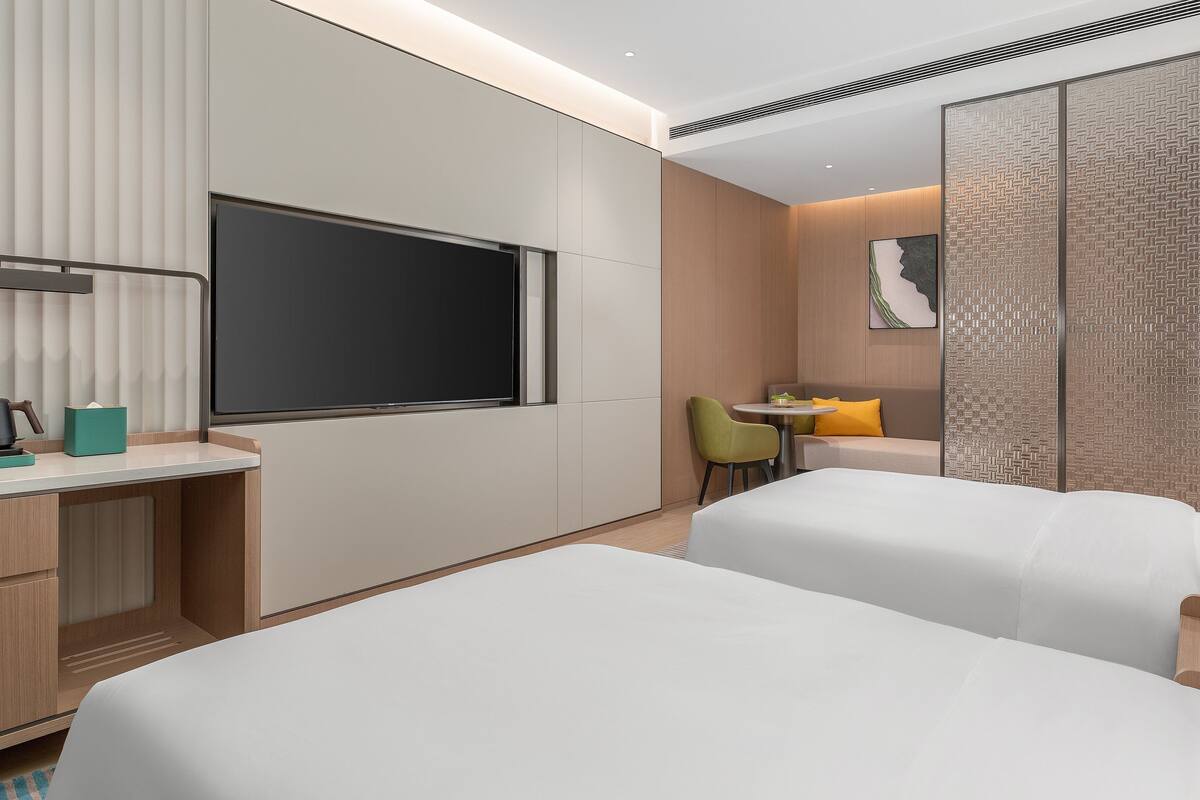 Une chambre d’hôtel moderne équipée de deux lits, d’un bureau avec une machine à café, d’une télévision et d’un coin repas comprenant une chaise et une table.