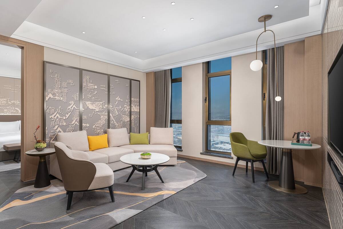 Une chambre d’hôtel moderne avec une grande fenêtre, un canapé, une petite table et un lit.