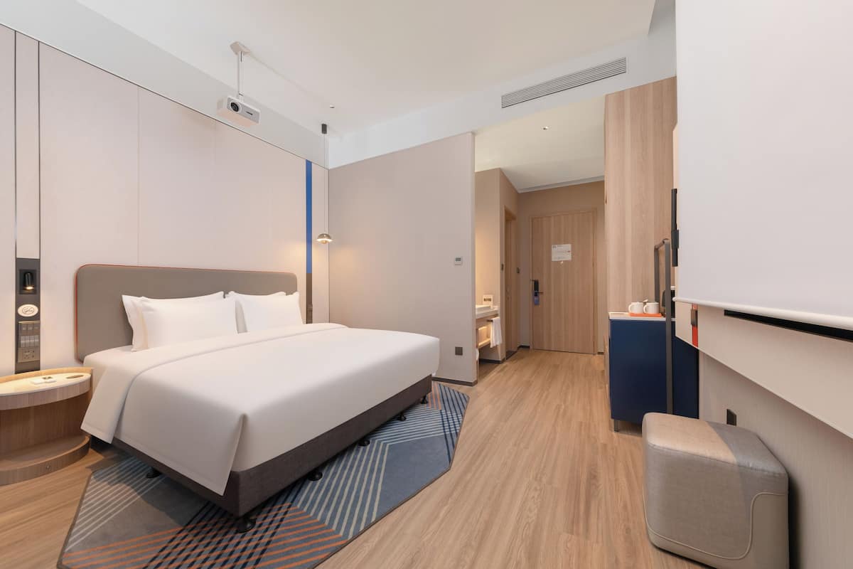 A modern hotel room with a large bed, a desk, and a television.