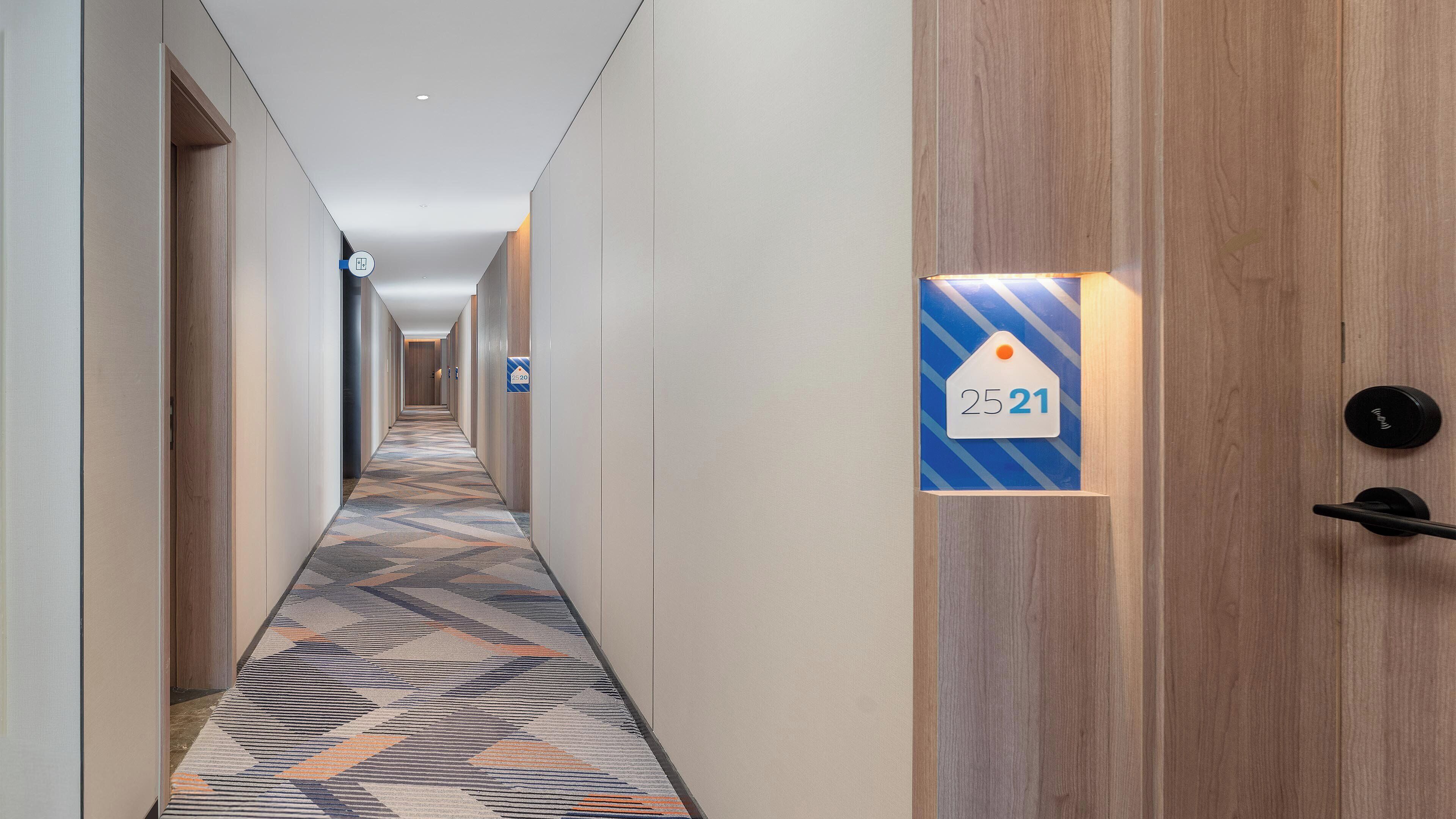 Un pasillo de hotel con alfombra estampada, paredes de madera y una puerta con el letrero del número de habitación 25,21.