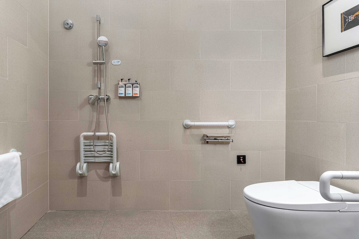 A modern bathroom with a walk-in shower, grab bars, a toilet, and a towel rack.
