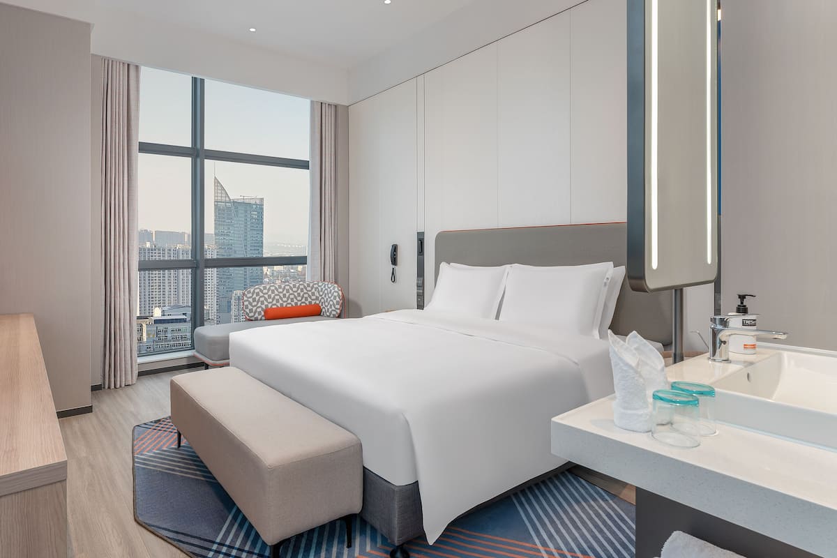 A modern hotel room with a large bed, a desk, a bathroom, and a city view.