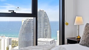 A hotel room with a large window offering a view of the ocean and tall buildings.