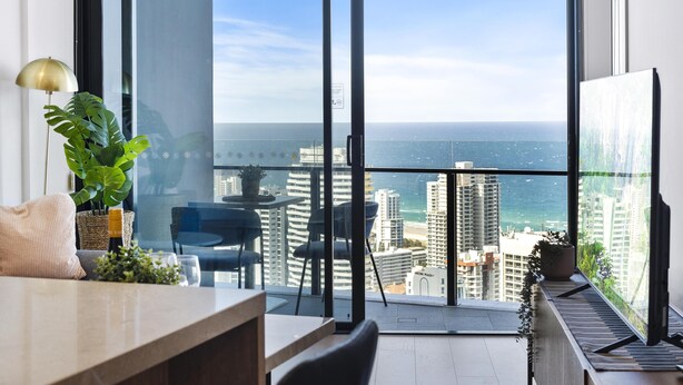 A modern living room with a large window overlooking a cityscape and the ocean.