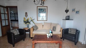 A living room with a wooden coffee table, two black sofas with leopard print cushions, a beige sofa, a chandelier, and a framed picture on the wall.