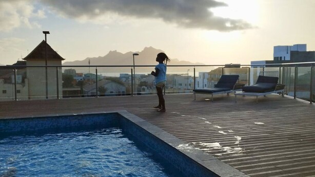 Zona de piscina en la azotea con vistas a montañas y edificios.