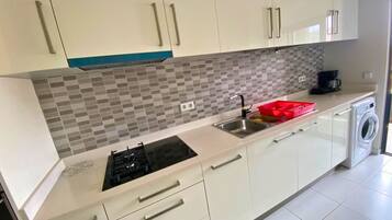 A modern kitchen with white cabinets, a tiled backsplash, a gas stove, a sink, and a washing machine.