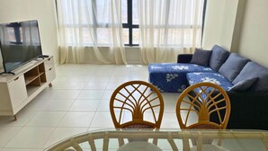 Una sala de estar con televisión, dos sillones de mimbre, un sofá y una mesa de vidrio.