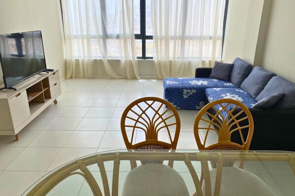 A living room with a TV, two wicker chairs, a sofa, and a glass table. - Sunset in Mindelo (Mindelo)