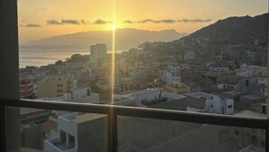 Vista desde una ventana con un paisaje urbano al atardecer, con edificios y una cadena montañosa distante.