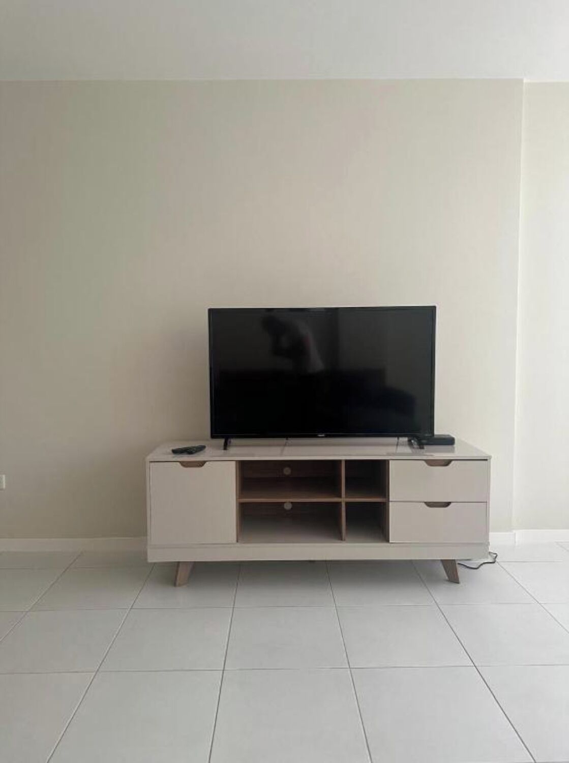 A white TV stand with a flat-screen TV, two remote controls, and a drawer.