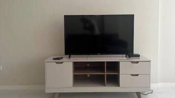 A white TV stand with a flat-screen TV, two remote controls, and a drawer.