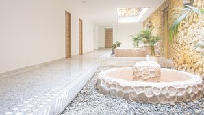 A spacious indoor area with a stone wall, a water feature, and a skylight. - Gardin home (Cali)
