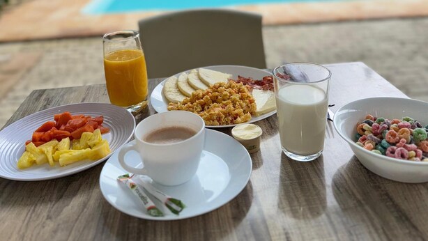 A breakfast table with plates of food, a glass of orange juice, a cup of coffee, and a bowl of cereal. - Gardin home (Cali)