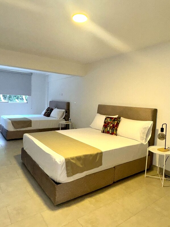 A hotel room with two beds, a small table, and a lamp.