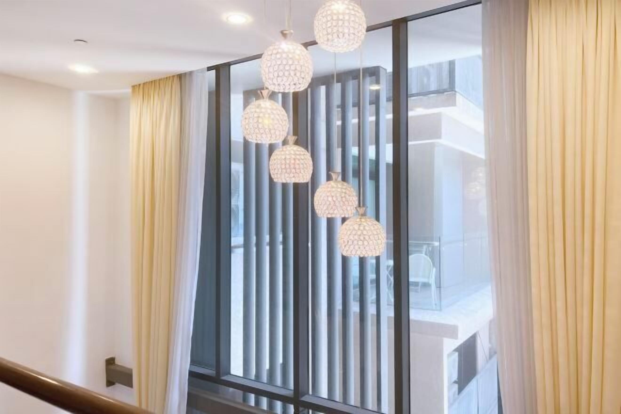 A modern interior with a staircase, a glass partition, and a row of spherical pendant lights.