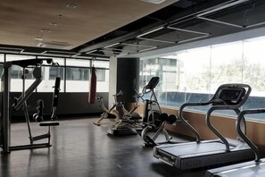 Un gimnasio con equipo de cardio, máquinas de pesas y un ventanal que proporciona luz natural.