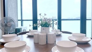 A dining table with white bowls and plates, a fan, and a potted plant with flowers. - Kwen Suites - City Centre Riverson Soho 2Br l Studio l Duplex (Kota Kinabalu)