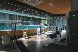 Een sportschool met trainingsapparatuur, een groot raam en uitzicht op een zwembad.