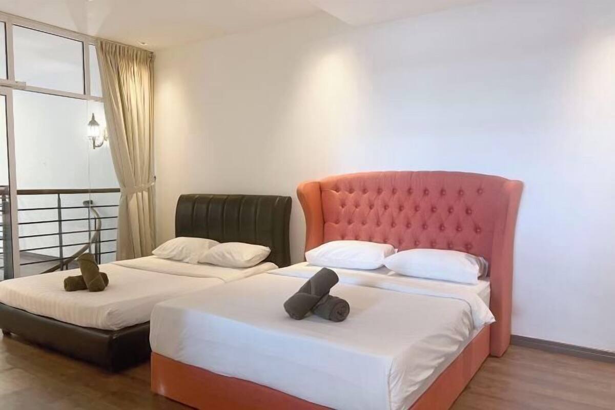 Ein Hotelzimmer mit zwei Betten, eines mit einem grünen Kopfteil und das andere mit einem rosafarbenen. Auf den Betten liegen Kissen und zusammengerollte Handtücher.