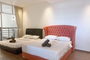 Une chambre d’hôtel avec deux lits, l’un avec une tête de lit verte et l’autre avec une tête de lit rose. Des oreillers et des serviettes roulées sont posés sur les lits.